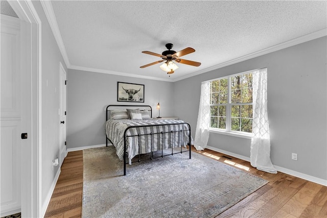bedroom with wood finished floors, ornamental molding, baseboards, a textured ceiling, and a ceiling fan