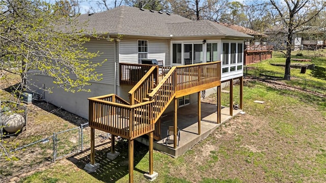 back of property with a wooden deck, a patio area, roof with shingles, a sunroom, and stairway
