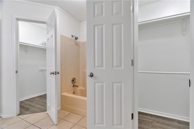 1740 Oxford Pl, Springdale, AR 72764 - bathroom with washtub / shower combination, a spacious closet, a textured ceiling, tile patterned floors, and baseboards