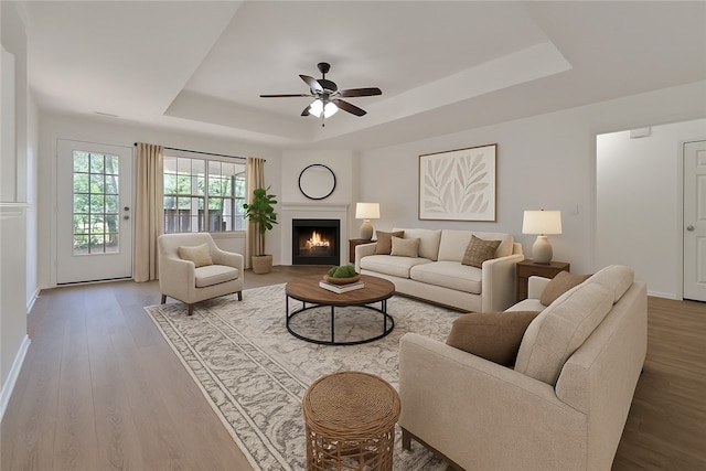 1765 Oxford Pl, Springdale, AR 72764 - living room featuring a tray ceiling, baseboards, wood finished floors, a ceiling fan, and a warm lit fireplace