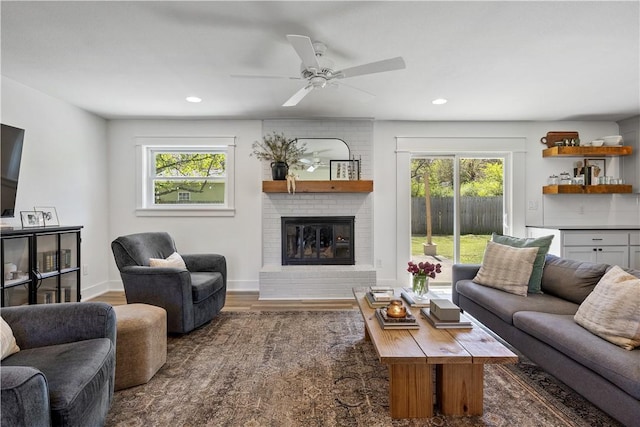 living area featuring a ceiling fan, a brick fireplace, wood finished floors, and plenty of natural light