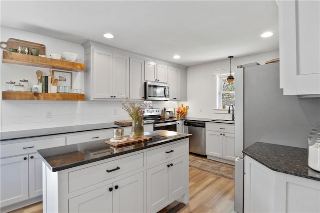 kitchen featuring open shelves, a sink, light wood-type flooring, backsplash, and appliances with stainless steel finishes