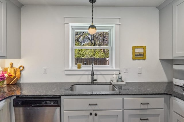 kitchen with stainless steel dishwasher, a sink, dark stone countertops, white cabinetry, and pendant lighting