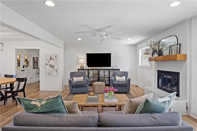 living room with baseboards, a brick fireplace, recessed lighting, and light wood-style floors