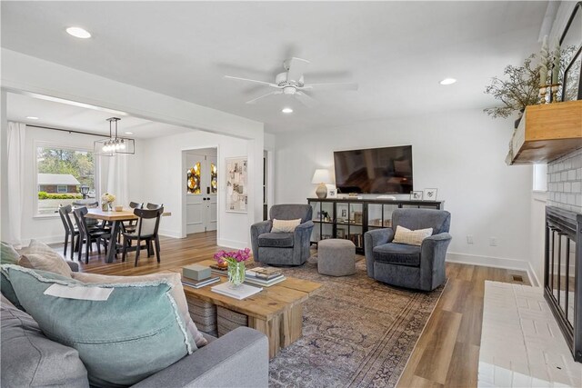 living room with ceiling fan with notable chandelier, wood finished floors, a fireplace, and recessed lighting