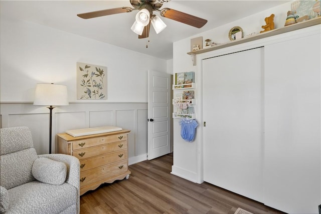 living area featuring wood finished floors, a wainscoted wall, and ceiling fan