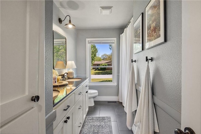 full bath with tile patterned floors, a sink, double vanity, toilet, and a textured wall