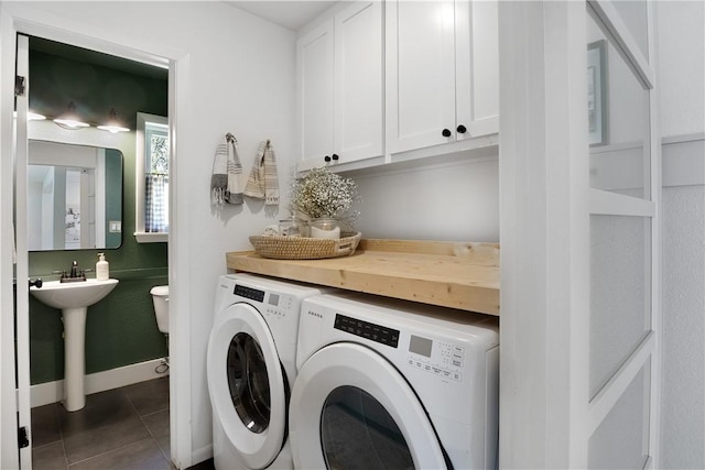 laundry area featuring washing machine and dryer, baseboards, cabinet space, and dark tile patterned flooring