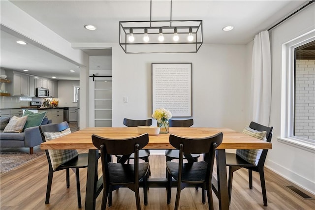 dining room featuring a barn door, light wood finished floors, baseboards, visible vents, and recessed lighting