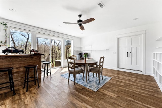 dining area with a ceiling fan, a dry bar, wood finished floors, and visible vents