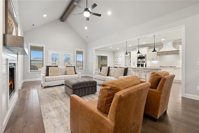 living area featuring beamed ceiling, baseboards, ceiling fan, a warm lit fireplace, and dark wood-type flooring