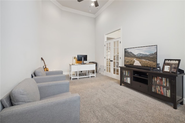 carpeted living area featuring french doors, a ceiling fan, baseboards, a towering ceiling, and ornamental molding