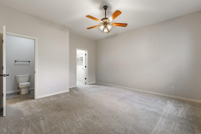 unfurnished bedroom featuring baseboards, carpet flooring, ceiling fan, connected bathroom, and a spacious closet