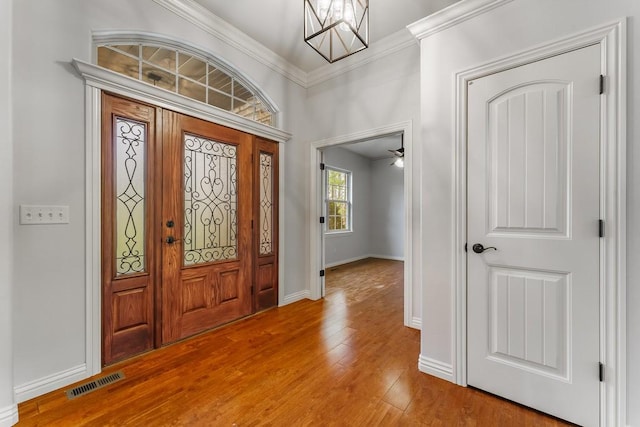 entrance foyer featuring wood finished floors, baseboards, visible vents, crown molding, and a notable chandelier