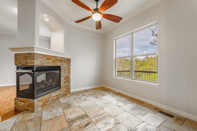 unfurnished living room with baseboards, ceiling fan, a stone fireplace, and crown molding