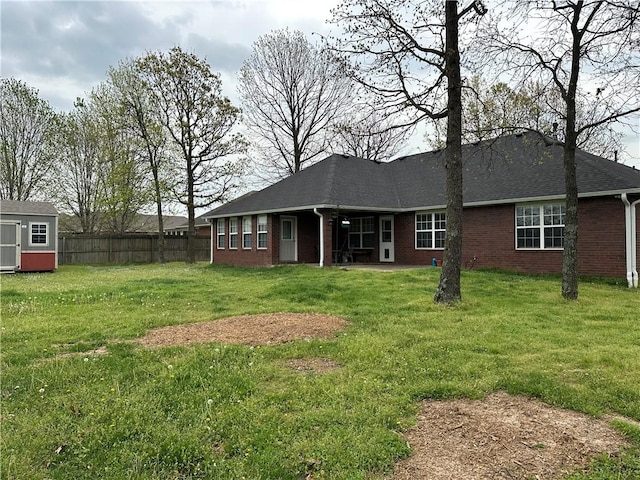 rear view of house featuring fence, a lawn, and brick siding