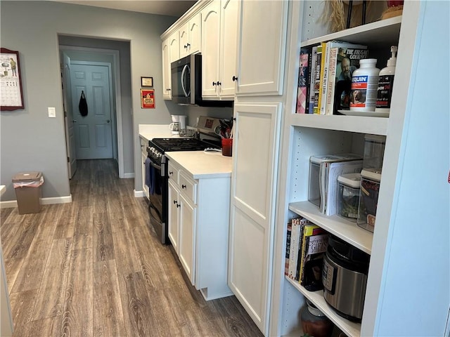 kitchen with stainless steel range with gas stovetop, baseboards, white cabinetry, wood finished floors, and light countertops