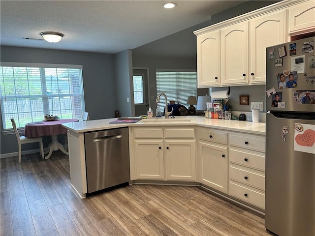 kitchen featuring a sink, light wood-type flooring, a peninsula, appliances with stainless steel finishes, and recessed lighting