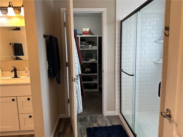 full bath featuring a shower stall, a walk in closet, vanity, and wood finished floors