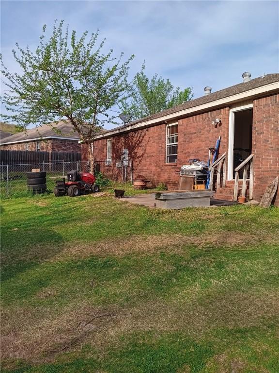 back of property featuring brick siding, entry steps, a lawn, and fence