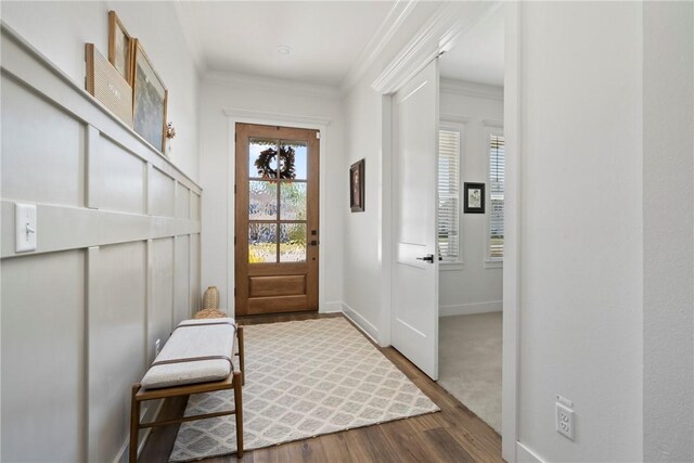 doorway with wood finished floors, ornamental molding, and baseboards