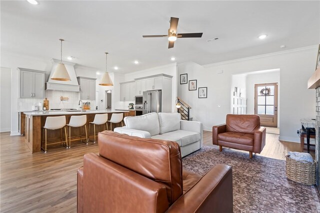 living area featuring a ceiling fan, light wood-style floors, baseboards, ornamental molding, and recessed lighting