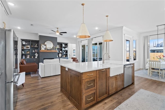 kitchen featuring appliances with stainless steel finishes, a sink, a ceiling fan, a center island with sink, and light countertops