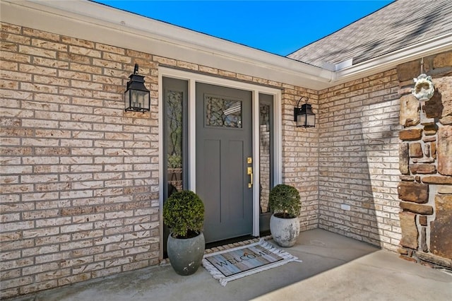 doorway to property with brick siding, a shingled roof, and covered porch