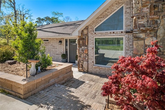 exterior space featuring stone siding, brick siding, and roof with shingles