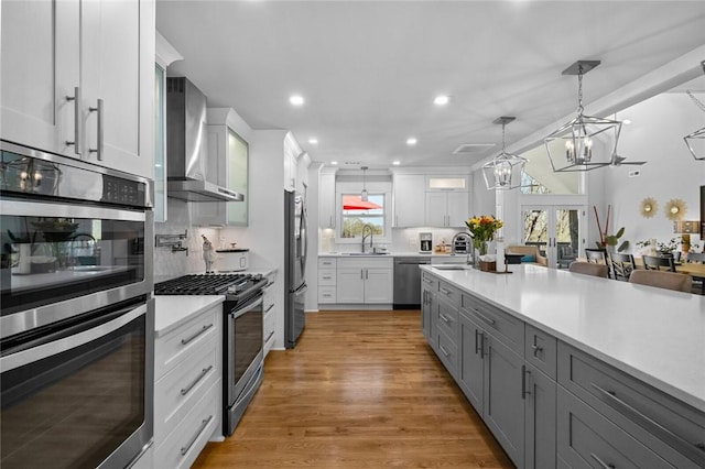 kitchen with light countertops, a sink, appliances with stainless steel finishes, and wall chimney range hood