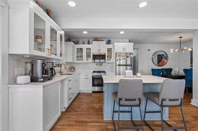 kitchen with stainless steel appliances, a kitchen breakfast bar, a sink, backsplash, and white cabinetry
