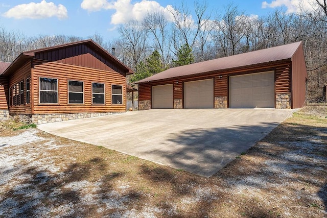 view of side of home featuring a detached garage, stone siding, board and batten siding, an outbuilding, and metal roof