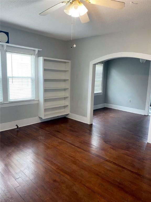 spare room featuring arched walkways, ceiling fan, baseboards, and dark wood-style flooring