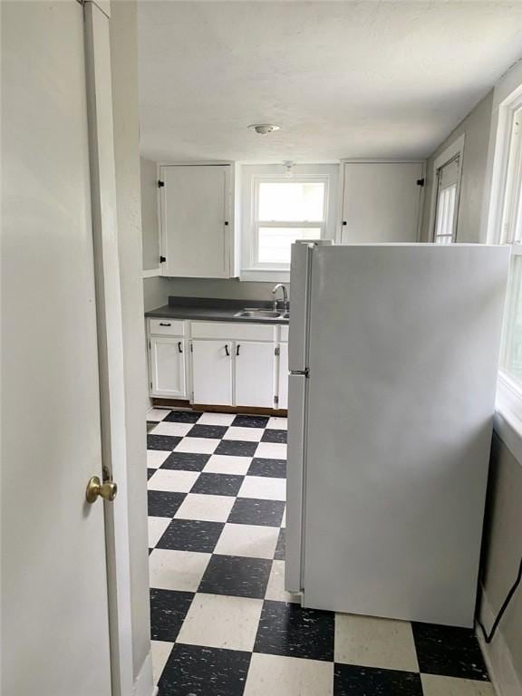 kitchen featuring dark floors, dark countertops, a sink, freestanding refrigerator, and white cabinetry