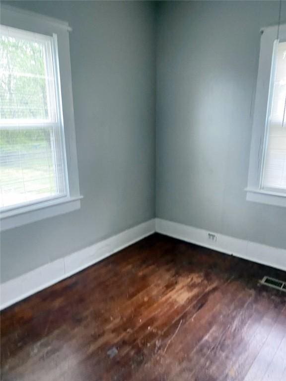 empty room with baseboards, dark wood-type flooring, visible vents, and plenty of natural light