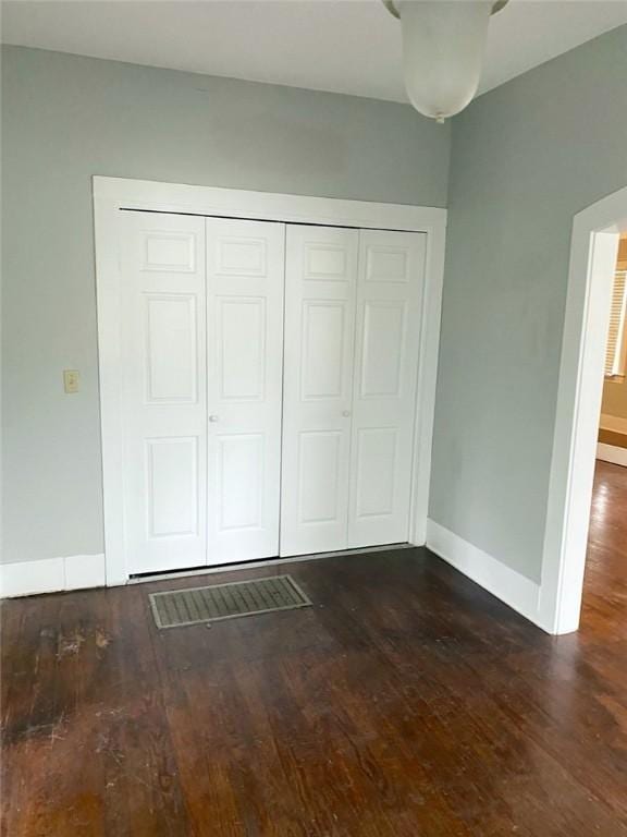 unfurnished bedroom with dark wood finished floors, a closet, and baseboards