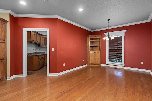 unfurnished dining area with light wood-style flooring, a textured ceiling, baseboards, and a notable chandelier