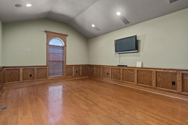 unfurnished living room with a textured ceiling, wainscoting, visible vents, lofted ceiling, and wood finished floors