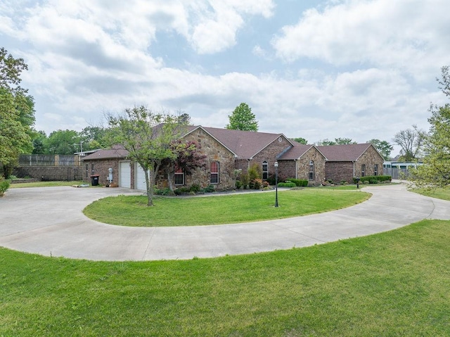 view of front of house featuring a front lawn, stone siding, concrete driveway, fence, and a garage