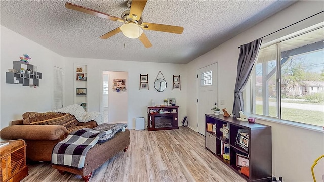 living room with ceiling fan, light wood finished floors, and a textured ceiling