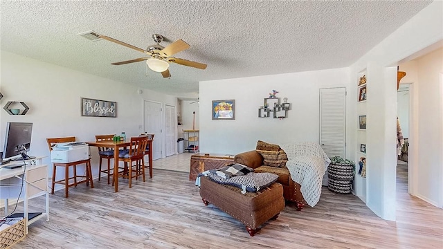 living room featuring a textured ceiling, ceiling fan, visible vents, and light wood-type flooring