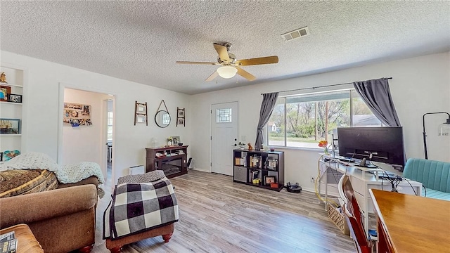 home office with ceiling fan, a textured ceiling, visible vents, baseboards, and light wood-style floors