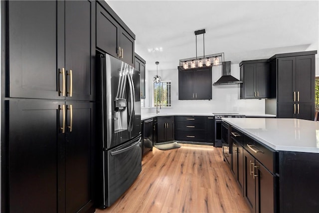 kitchen with wall chimney exhaust hood, light wood-style floors, light countertops, decorative light fixtures, and appliances with stainless steel finishes