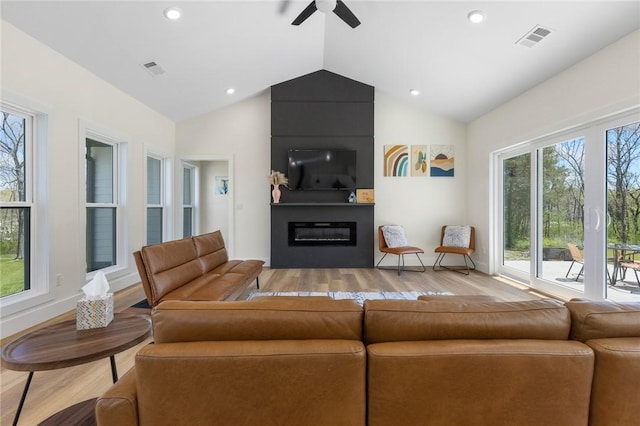 living room featuring light wood-style floors, ceiling fan, a large fireplace, lofted ceiling, and visible vents