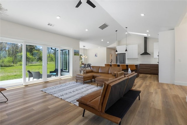 living area featuring vaulted ceiling, visible vents, light wood finished floors, and a ceiling fan