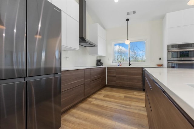 kitchen with stainless steel appliances, visible vents, white cabinetry, modern cabinets, and wall chimney range hood