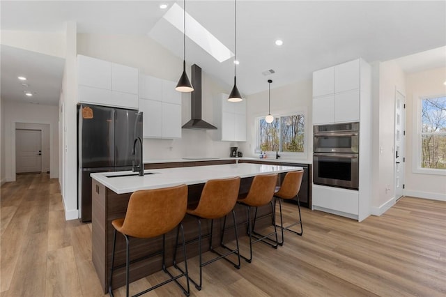 kitchen featuring modern cabinets, wall chimney range hood, appliances with stainless steel finishes, and a kitchen island with sink