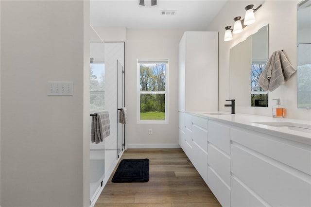 bathroom with a sink, double vanity, visible vents, wood finished floors, and a shower stall
