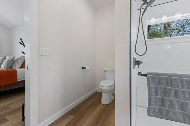 ensuite bathroom featuring a tile shower, wood finished floors, toilet, ensuite bath, and baseboards