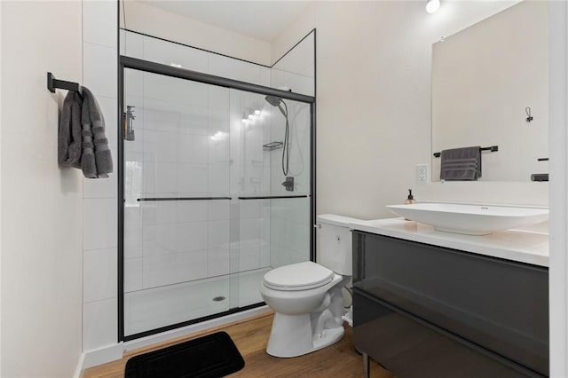 bathroom with toilet, wood finished floors, vanity, and a stall shower